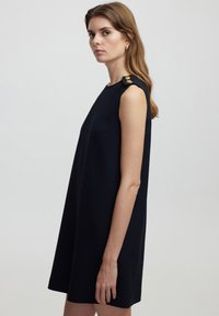 Vestido sin mangas de color navy con un corte sencillo, que cuenta con detalles en los hombros adornados con botones dorados y una tela suave y texturizada.