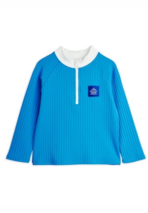 Blå langærmet skjorte med lodrette striber, hvid krave, hvid halv-lynlås og et lille blåt mærke med teksten "The Inter Galactic Travel Agency" foran.