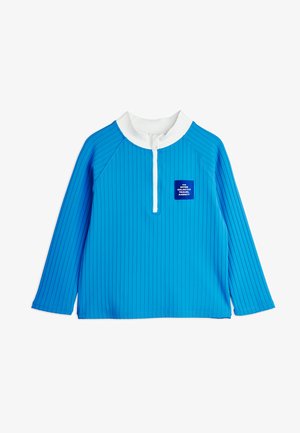 Blue long-sleeve shirt with vertical stripes, white collar, white half-zip, and a small blue patch reading "The Inter Galactic Travel Agency" on front.