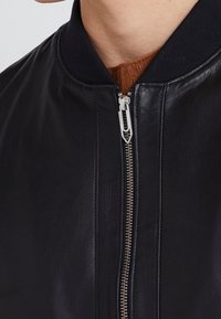 Czarna skórzana kurtka typu bomber z zamkiem błyskawicznym, ściągaczem na kołnierzu i gładką fakturą. Minimalistyczny design bez widocznych wzorów i ozdób.