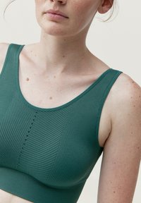 Tyrkysový žebrovaný bralet s širokými ramínky, který se vyznačuje hladkým povrchem a vertikálním švem. Bez vycpávek nebo viditelné kovové součásti.