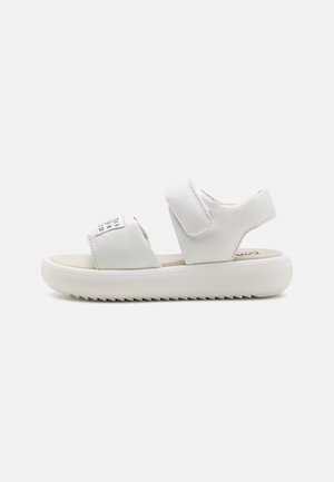 Sandalias blancas de material sintético suave con correas ajustables de Velcro, plantilla acolchada y suela de goma texturizada.