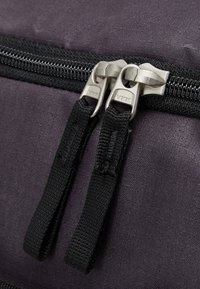Primo piano di uno zaino in tessuto nero con zip doppia YKK, caratterizzato da hardware metallico argento e superficie in tessuto testurizzato.