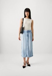 Lichtgewicht geribd tanktop in crème, gecombineerd met een lichtblauwe denim rok van middellange lengte. Accessoires zijn een kleine zwarte handtas en hakken.