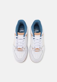White athletic sneakers with blue and tan accents, featuring a textured leather upper, padded collar, and a perforated toe for breathability.