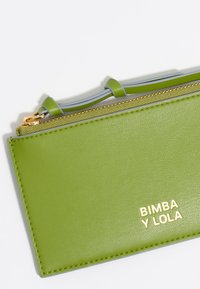 Zielona skórzana portmonetka Bimba y Lola ma gładką fakturę, złote akcesoria i szary zamek błyskawiczny. Projekt obejmuje obszyte krawędzie.