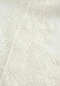 Tissu en dentelle blanche mettant en avant des motifs floraux et des détails délicats, contrastant avec un fond en satin lisse de teinte crème.