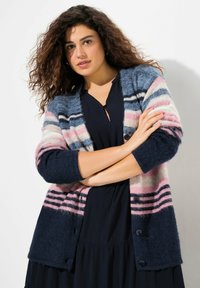 Randig cardigan i marinblått, rosa och ljusblått. Mjuk textur, knappstängning och ribbade ärmslut. Bärs över en mörk klänning.