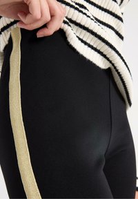 Sorte leggings med et slankt design, der har en gylden metallisk side stripe. Stoffet virker glat og strækkeligt, hvilket øger komforten.