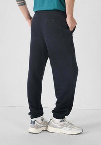 Zwarte sweatpants van zachte stof, met een elastische tailleband, opgerolde enkels en een enkele achterzak met een knoop.