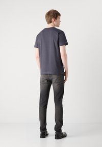 Sötétszürke pamut póló rövid ujjakkal és kerek nyakkivágással, fekete, slim-fit farmernadrággal és fekete cipővel párosítva, hátulról nézve.