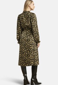 Abito con stampa leopardata in tessuto setoso, lunghezza media, con cintura in vita, maniche lunghe e dettagli arricciati sulle spalle. Stivali neri alti fino al ginocchio.