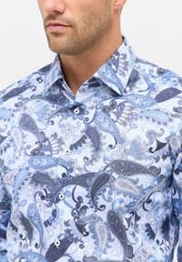 Een knoopsluiting shirt met een lichtblauwe achtergrond, voorzien van complexe donkerblauwe paisley patronen, contrasterende witte knopen en een gestructureerde kraag.