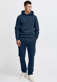 Dunkelblaues Hoodie- und Jogginganzug-Set aus weichem Stoff, mit Kängurutasche, gerippten Bündchen und elastischem Bund. Weiße Sneakers.