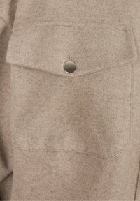 Poche en tissu beige avec un rabat arrondi et une fermeture pression métallique unique. Texture douce avec un motif chiné subtil.