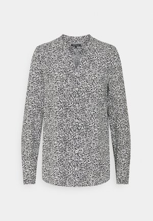 Blouse à manches longues en noir et blanc avec un col en V et des détails de boutons ; présente un motif de points éparpillés sur un tissu léger.