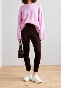 Pink fluffy sweater with long sleeves, paired with black fitted pants and white sneakers. Holding a small black handbag.