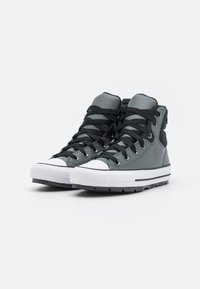 Grå högtoppsneakers med svarta snören, med en vit gummitå och sula, utställda mot en enkel vit bakgrund.