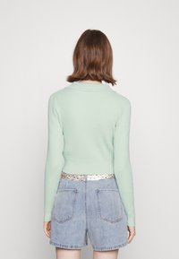 Sweater canelado verde menta com colarinho, design ajustado, mangas longas, combinado com calções de ganga de cintura alta azul claro com bolsos.