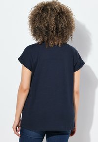 Camiseta de manga corta azul marino con puños enrollados, un ajuste relajado y un dobladillo redondeado. Textura suave sobre un fondo liso.