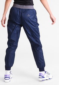 Marineblaue, leichte, knöchellange Sporthosen mit einem elastischen Bund und gerippten Bündchen. Mit einem kleinen Logo auf der Rückseite.