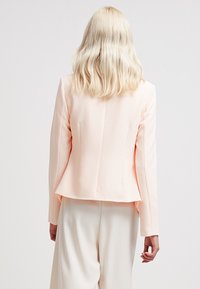 Różowa, dopasowana marynarka o wąskim kroju, z długimi rękawami i rozcięciem z tyłu. Gładka faktura, minimalistyczny design i brak widocznych elementów metalowych.