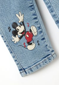 Vaqueros de mezclilla con un colorido dibujo de Mickey Mouse bailando rodeado de notas musicales en la pierna.