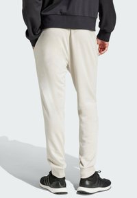Ljusbeiga joggingbyxor för herrar med en avsmalnande design, elastiska manschetter och sidofickor, i kombination med svarta träningsskor. Mjuk tygtextur.