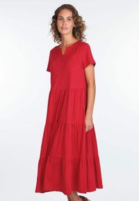 Rotes, gestaffeltes Kleid aus leichtem Stoff. Kurze Ärmel, V-Ausschnitt, weiche Textur, fällt unter das Knie und hat eine fließende Silhouette.