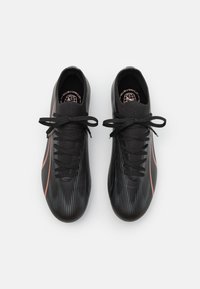 Scarpe sportive nere con una parte superiore testurizzata, caratterizzate da righe verticali, una striscia di accento rosa e lacci tradizionali.