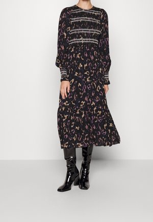 Femme portant une robe midi noire à manches longues avec une taille et des poignets froncés, associée à des bottes noires brillantes montant jusqu'aux genoux.