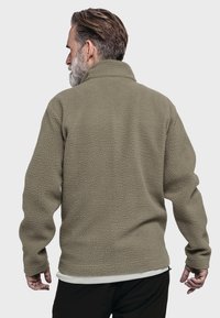 Fleece-Jacke in olivgrün mit strukturierter Oberfläche, hohem Kragen und langen Ärmeln. Verfügt über eine Reißverschlusstasche an der Seite.