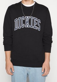 Felpa nera con ricamo bianco e blu navy della scritta "DICKIES". Presenta un collo tondo e polsini e orlo a coste. Vestibilità casual.