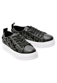 Sneakers neri con una punta in pelle liscia e pannelli laterali testurizzati decorati con un motivo di borchie argentate. La suola è bianca e spessa.