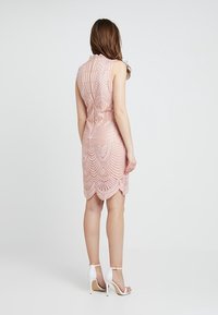 Robe rose clair sans manches avec un travail de perles complexe et un ourlet festonné. Le design présente des motifs géométriques, associée à des escarpins blancs.