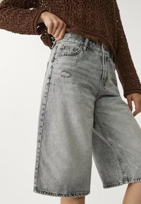 Bermudas de mezclilla gris claro con un corte relajado, que presentan detalles desgastados y costuras en contraste. Diseño de cinco bolsillos con cierre de botón.