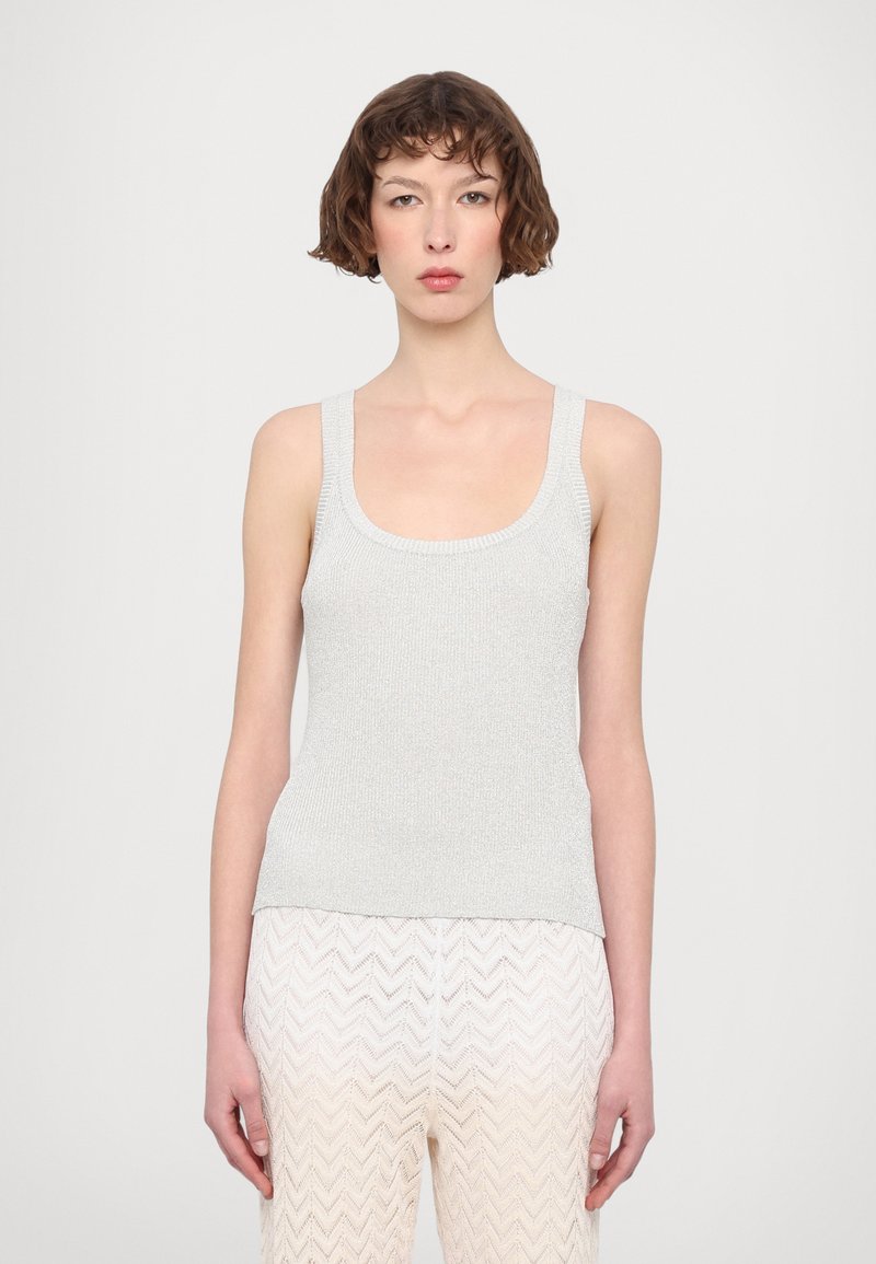 Top sin mangas de color gris claro con tachuelas anchas y un escote redondeado, combinado con pantalones de textura crema con patrón en zigzag.