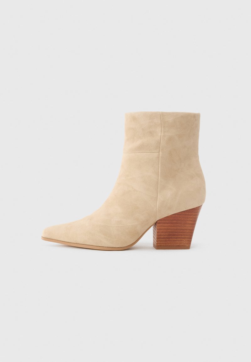 Béžová semišová kotníková bota s špičatou špičkou, konturovaným svrškem a zúženým dřevěným podpatkem. Hladký povrch bez viditelných vzorů nebo akcentů.