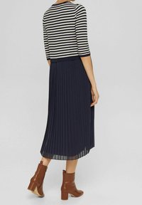 Randig tröja, veckad marinblå kjol, bruna anklarstövlar med blockklackar. Klädseln har strukturerad stickning och slät tyg.