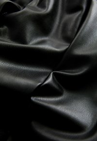 Tissu en cuir noir froissé avec une surface lisse, légèrement brillante et une texture à grain fin visible en gros plan.