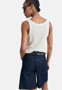 Lys grå tanktop med brede stropper, parret med mørke denim shorts med baglommer og kontrastsyning, set bagfra.