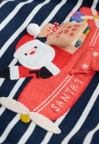 Rødt og marineblåt stribet stof med broderet julemand på et legetøjsfly, med gaver og karamelliserede sukkerrør, inklusive en hvid pompom-detalje.