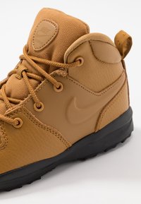 Sneaker alta in pelle marrone e tessuto con superficie strutturata, suola in gomma nera e un logo ben visibile sul lato.