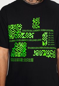 Camiseta negra con un diseño gráfico en verde brillante. El diseño incluye código binario, patrones de cuadros y texto en varias disposiciones.