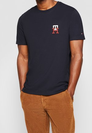 Marineblaues Baumwoll-T-Shirt mit rundem Ausschnitt, kurzen Ärmeln und gesticktem Logo in Rot und Weiß auf der Brust. Glatte Textur, legerer Schnitt.