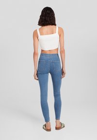Blå skinny jeans med hög midja, kombinerad med en vit, räfflad croptop. Jeansarna har bakfickor och en figurnära design.