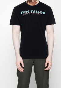 Černé bavlněné tričko s logem "TOM TAILOR Essentials" v tyrkysovém a růžovém písmu. Kulatý výstřih a krátké rukávy.