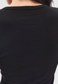 Svart ribbad kortärmad topp med rund halsringning. Tyget har vertikala linjer som ger en texturerad look.