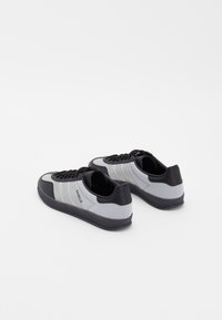Gray and black sneakers with a textured mesh upper, three horizontal white stripes, round laces, and a rubber sole.