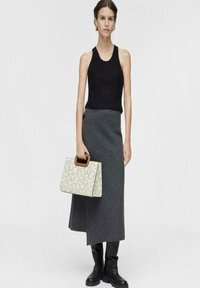 Top negro sin mangas, falda de lana gris, botas altas negras hasta la rodilla, sosteniendo un bolso crema con un diseño estampado y mango marrón.